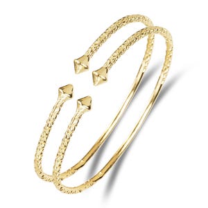 May include: Two gold bangle bracelets with a textured diamond pattern and pointed ends.