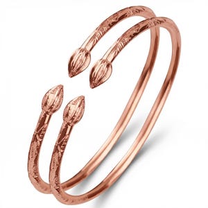 May include: Two rose gold bangles with floral and leaf detailing. Each bangle features a bud-shaped end. The bangles are made of a shiny, metallic material and are displayed against a white background.