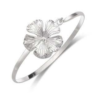 May include: A silver bangle bracelet with a delicate flower charm. The flower is textured and has a slightly raised center.
