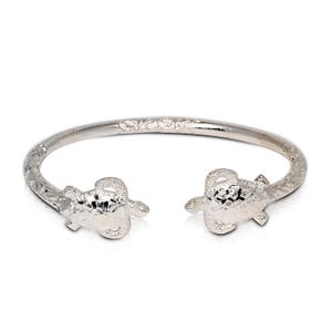 May include: Silver bangle bracelet with two turtle charms. The bracelet is engraved with a floral pattern.