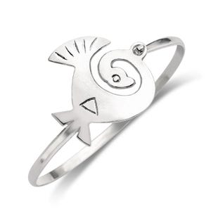 May include: A silver bracelet with a stylized bird design. The bird has a spiral pattern on its body and a small circle in the center.