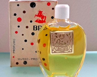 May include: Vintage perfume bottle with a white cap and a gold label. The bottle is filled with a yellow liquid and sits in front of a box with red, black, and brown polka dots. The box has the text "BP" and "PROFUMO".