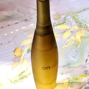 Könnte beinhalten: Eine hohe, schlanke Flasche aus mattiertem, bernsteinfarbenem Glas mit verjüngtem Hals und passendem Verschluss. Das Wort "onella" ist in kleinen, dunklen Kleinbuchstaben auf der Vorderseite der Flasche aufgedruckt, die eine glatte, längliche Form hat.