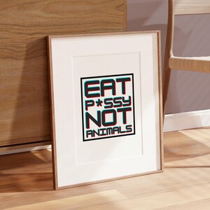 May include: Framed art print with the text "EAT P*SSY NOT ANIMALS" in a bold, 3D-style font. The words are in a black box with a white border, set against a white background. The frame is a light brown color.