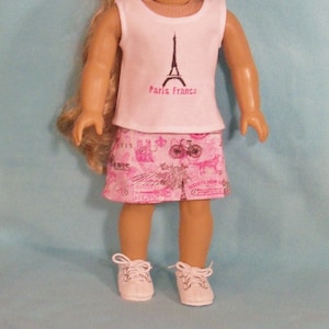 May include: A white sleeveless shirt with a black Eiffel Tower graphic and the text "Paris France". The shirt is paired with a pink skirt featuring a Parisian-themed print with bicycles, flowers, and the word "Paris".