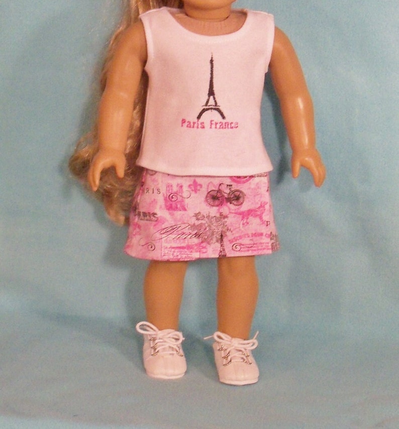 May include: A white sleeveless shirt with a black Eiffel Tower graphic and the text "Paris France". The shirt is paired with a pink skirt featuring a Parisian-themed print with bicycles, flowers, and the word "Paris".