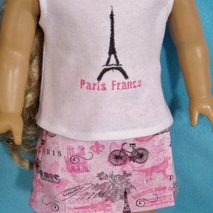 May include: A white sleeveless shirt with a black Eiffel Tower graphic and the text "Paris France" in pink. The shirt is paired with a pink skirt featuring a Parisian-themed print with bicycles, roses, and the word "Paris".
