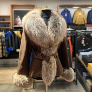 May include: A brown suede jacket with a large fur collar and cuffs. The jacket features a matching belt and fur trim along the front. The jacket is displayed on a mannequin in a clothing store.