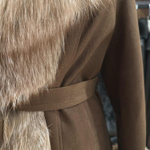 May include: A brown coat with a fur collar and trim. The coat has a belt at the waist and a textured pattern on the fabric. The fur is a light brown color, and the coat appears to be made of leather or a similar material.