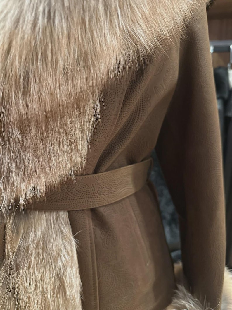 May include: A brown coat with a fur collar and trim. The coat has a belt at the waist and a textured pattern on the fabric. The fur is a light brown color, and the coat appears to be made of leather or a similar material.