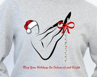 May include: Gray sweatshirt with a graphic of a hand holding a Santa hat, a red bow, and a string of Christmas lights. The text "May Your Holidays Be Balanced and Bright" is printed in red.
