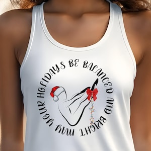 May include: White tank top with a circular graphic. The graphic features a hand with a Santa hat, a red bow, and string lights. The text around the graphic reads "May your holidays be balanced and bright."