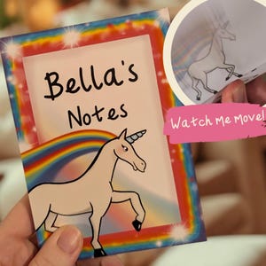 May include: A notebook featuring the text "Bella's Notes" and a unicorn illustration. The notebook has a rainbow and star-filled border. A smaller image shows a unicorn in motion with the text "Watch Me Move!"