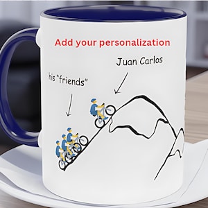 May include: White ceramic mug with a blue interior and handle. The mug features a mountain biking illustration with the text "Add your personalization" and "Juan Carlos". Below the illustration is the text "his 'friends'".