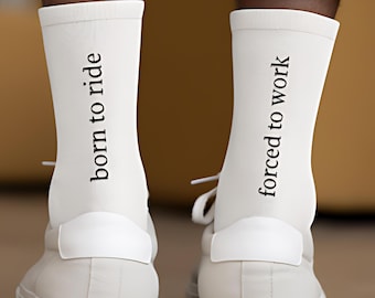 May include: White socks with the text "born to ride" and "forced to work" in black. The socks are worn with white sneakers. The image shows the back of the legs and feet.