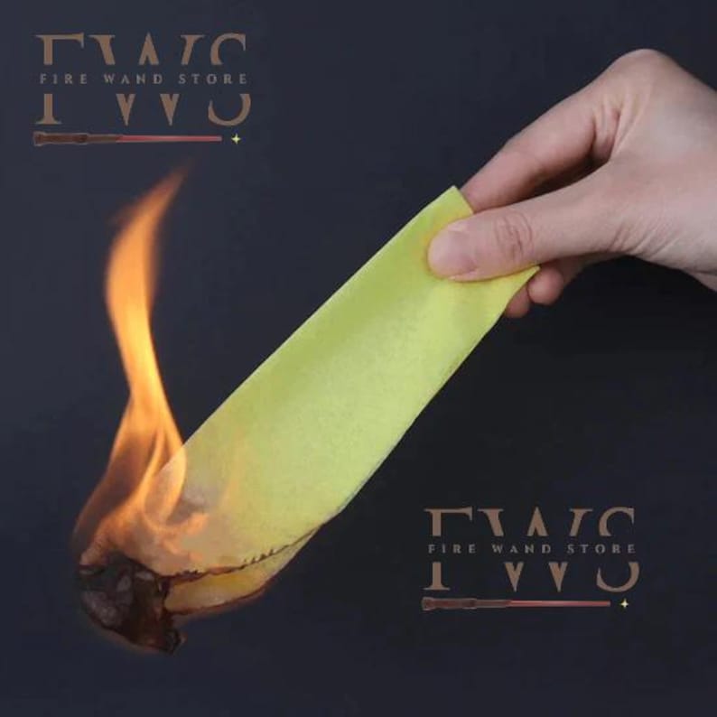 May include: A hand holds a yellow strip of material, with flames engulfing the bottom edge. The image has the text "FIRE WAND STORE" and a wand graphic. The background is a dark, solid color.