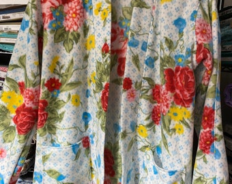 May include: A white fleece robe with a floral print featuring red, yellow, and blue flowers. The robe has a shawl collar and two pockets.