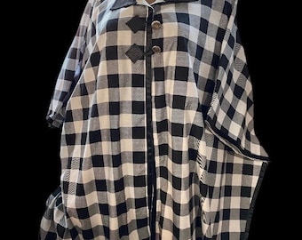 May include: A black and white checkered button-up shirt with a black collar and black trim. The shirt has a loose fit and a long, flowing style.