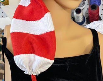 May include: A red and white striped hat with a white pom-pom at the end. The hat is made of a soft material and has a long, pointed shape. A red ribbon is attached to the hat. The hat is likely a costume or novelty item.