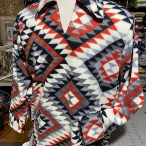 May include: A long-sleeved shirt with a geometric pattern in shades of red, black, white, and gray. The shirt has a V-neck collar and a relaxed fit.