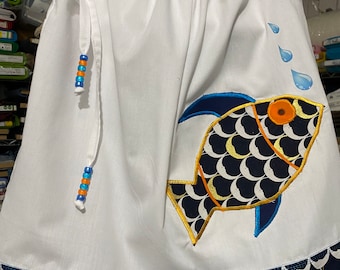 May include: White sleeveless dress with a blue and yellow fish design and a blue and gold trim. The dress has a drawstring neckline and blue and orange beads on the straps.