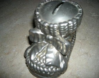 May include: A silver metal piggy bank shaped like a baby shoe with a ribbon and a slot on the top.
