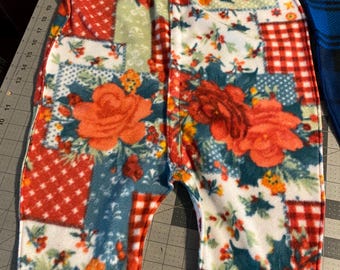 May include: A patchwork fleece baby wearable blanket with a floral and geometric pattern. The design features large red roses, red polka dots, and red and white gingham checks on a white, teal, and blue background. The blanket has a hood and a zipper closure.