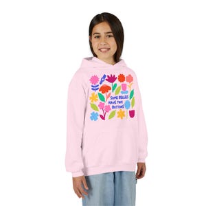 May include: A light pink hooded sweatshirt featuring a colorful graphic print of various stylized flowers and leaves in shades of red, blue, yellow, and pink, with the text "SOME BELLIES HAVE TWO BUTTONS" printed in blue in the center.
