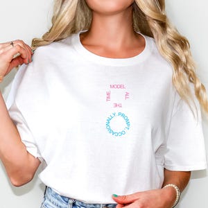 May include: White t-shirt with a crew neck featuring the text "All the time, occasionally prompt, model." The text is arranged in a circular and vertical pattern, with pink and blue lettering. The shirt is made of a soft, lightweight fabric.