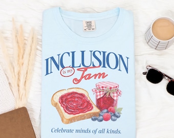 May include: Light blue t-shirt with the words "INCLUSION is my Jam" in blue and red script. The graphic includes a slice of toast with jam, a jar of jam, and berries. The text "Celebrate minds of all kinds" is at the bottom.