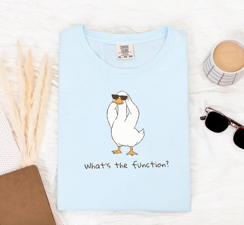 K&ouml;nnte beinhalten: Hellblaues Comfort Colors T-Shirt mit einer Cartoon-Ente, die eine Sonnenbrille tr&auml;gt und sich den Kopf h&auml;lt. Der Text "What's the function?" ist darunter gedruckt. Das Shirt ist XL-TG-EG.