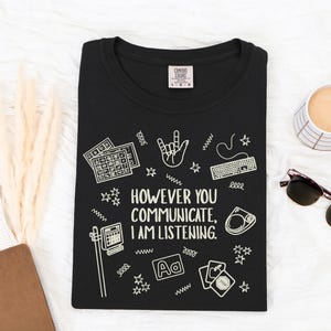 May include: Black t-shirt with the text "HOWEVER YOU COMMUNICATE, I AM LISTENING." and various white graphic icons. The shirt has a crew neck and a Comfort Colors tag.