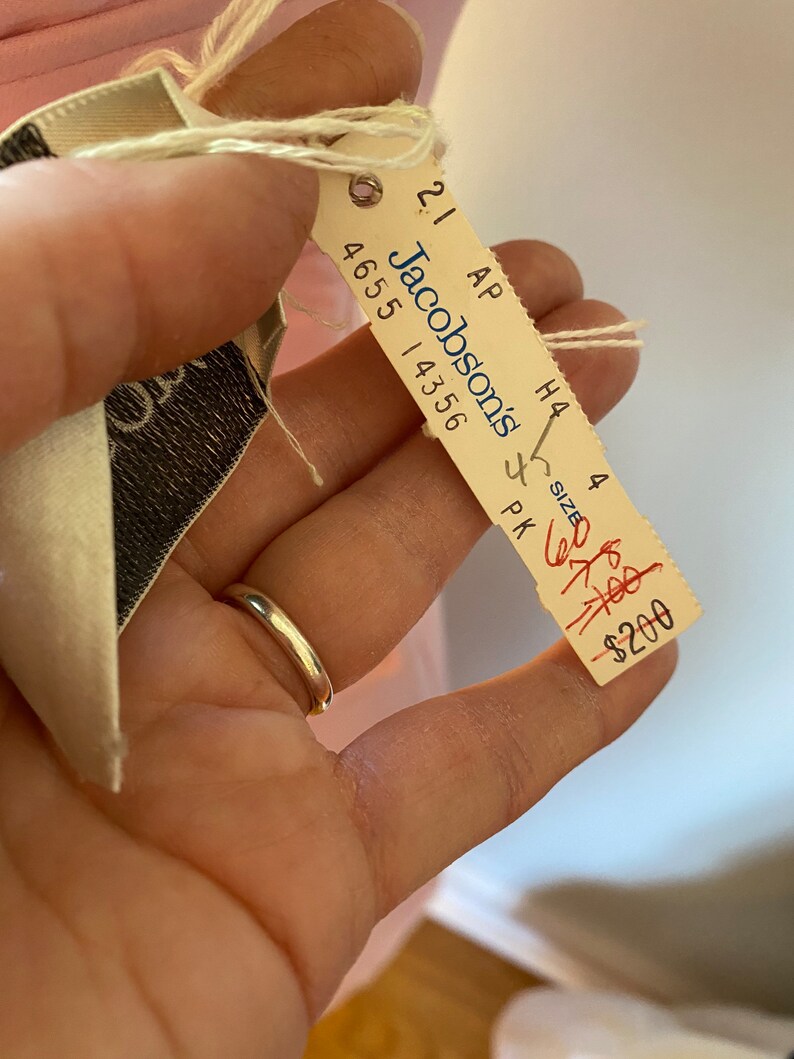 May include: A white tag with black text that reads "Jacobsons" and "4655 14356". The tag is attached to a pink fabric with a string. The tag also has the text "21 AP H4 4 SIZE PK" and a red handwritten price tag that reads "$200".