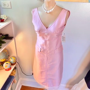 May include: A sleeveless pink dress with a v-neckline and a pearl necklace. The dress has a small pocket on the front and a white tag with the word "Anthropologie" on it.