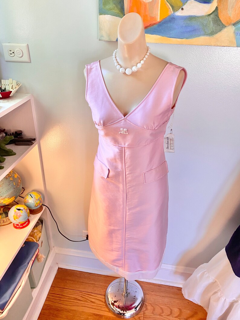 May include: A sleeveless pink dress with a v-neckline and a pearl necklace. The dress has a small pocket on the front and a white tag with the word "Anthropologie" on it.
