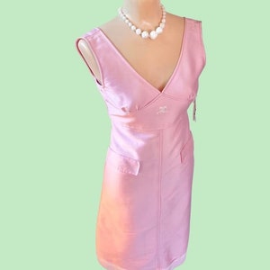 May include: A pink sleeveless dress with a V-neckline and a white embroidered logo. The dress has a fitted bodice and a straight skirt. The dress is on a white mannequin with a pearl necklace.