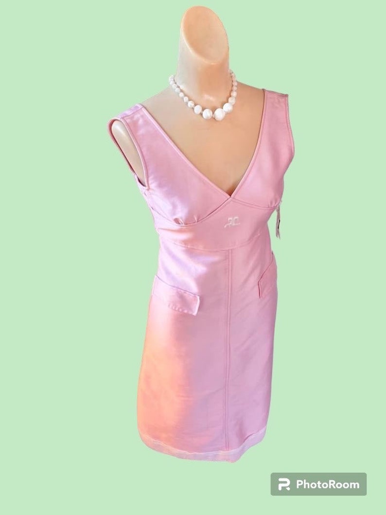 May include: A pink sleeveless dress with a V-neckline and a white embroidered logo. The dress has a fitted bodice and a straight skirt. The dress is on a white mannequin with a pearl necklace.