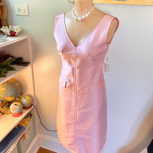May include: A sleeveless pink dress with a V-neckline and a white pearl necklace. The dress has a small pocket on each side and a white label with the text "Goodwill" on the right side.
