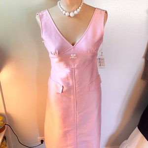 May include: A pink sleeveless dress with a V-neckline and a white pearl necklace. The dress has a small embroidered logo on the front and two pockets on the sides. The dress is on a mannequin.