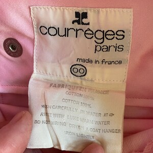 May include: White care label with black text for a pink Courr&egrave;ges Paris garment. The label reads "Fabriqu&eacute; en France", "Cotton 100%", "Wash carefully in water at 40&deg;", "Rinse with luke warm water", "Do not wring, dry on a coat hanger", "Iron lightly".