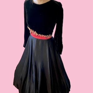 May include: A black velvet dress with a full skirt and a pink and gold embroidered belt.