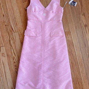 May include: A sleeveless pink dress with a white embroidered logo on the front. The dress has a v-neckline and a white trim at the hem.