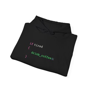 May include: Black hoodie with the text "if tired { drink_coffee(); }" in a coding-style font. The text is in white, pink, and green. The hoodie has a drawstring hood and is folded.