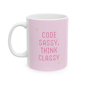 Peut inclure: Une tasse en céramique blanche avec un fond rose et le texte "CODE SASSY, THINK CLASSY" en lettres roses. Il y a deux petites étoiles dorées sur la tasse.