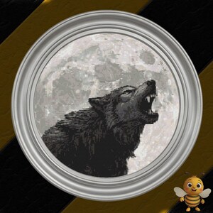 Puede incluir: Un bordado de punto de cruz redondo enmarcado que representa un lobo aullando contra una luna llena. El lobo está representado en tonos negros y grises, con la boca abierta aullando. La luna es blanca brillante y texturizada. El marco es plateado.