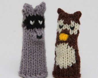 May include: Two knitted finger puppets, one is a raccoon with a black mask and the other is an owl with a yellow beak and white belly.