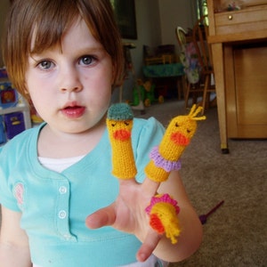 May include: A young person wearing a light blue shirt is playing with three finger puppets. The puppets are yellow with orange beaks and have different colored accents.