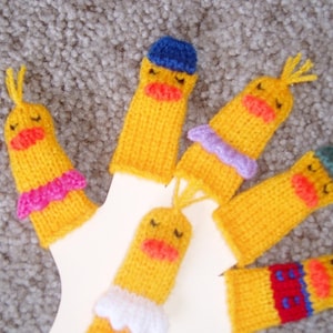 May include: Five yellow knitted finger puppets with different colored accents. The puppets have a duck-like appearance with closed eyes and a red beak. The accents include a blue hat, a purple bow, a green hat, a white collar, and a red and blue striped shirt.