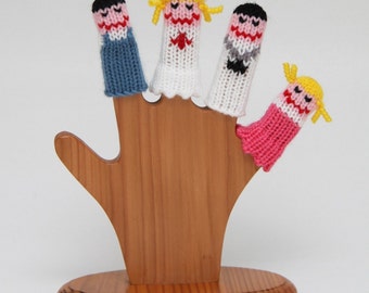 May include: Four knitted finger puppets on a wooden stand. The puppets are a bride, a groom, a bridesmaid, and a groomsman. The puppets are all wearing different colored clothing and have different facial expressions.