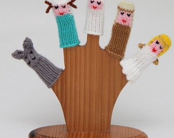 May include: Set of five knitted finger puppets on a wooden stand. The puppets include a sheep, an angel, a shepherd, a donkey, and a star. The puppets are all white with different colored accents.